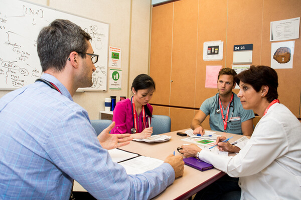 Several physicians sitting around a table talking with paperwork in front of them