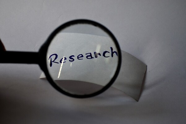 A piece of white paper with the word 'Reseach' written on it, behind a magnifying glass