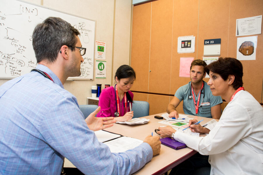 Several physicians sitting around a table talking with paperwork in front of them
