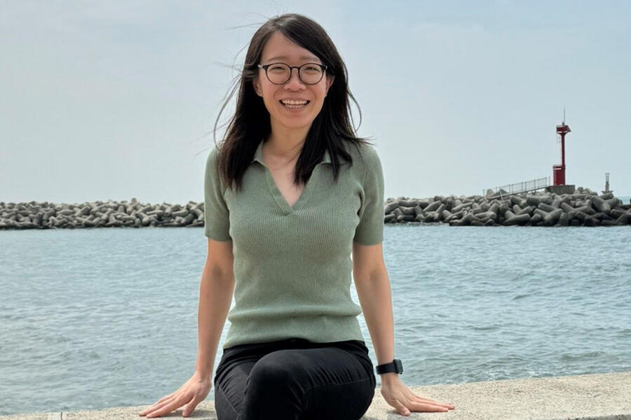 Photo of Dr. Carolyn Tan sitting on a ledge in front of a body of water.