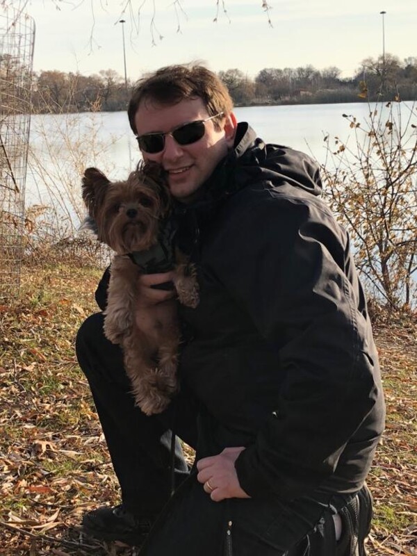 man crouching with small dog in front of lake