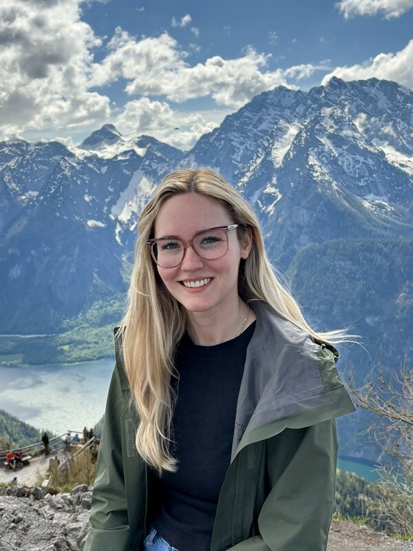 white woman with long blonde hair and glasses, with mountains in background