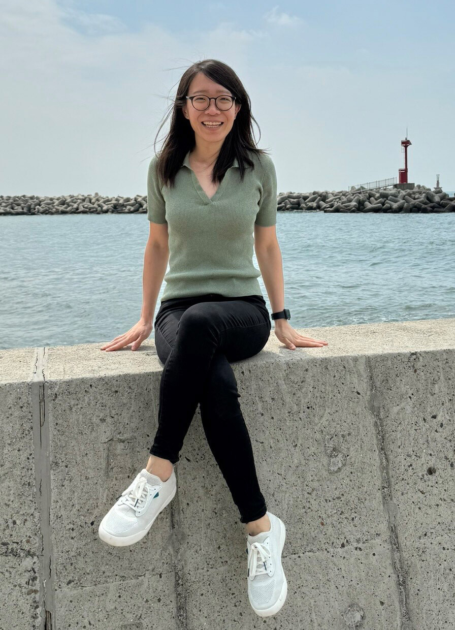 Photo of Dr. Carolyn Tan sitting on a ledge in front of a body of water.