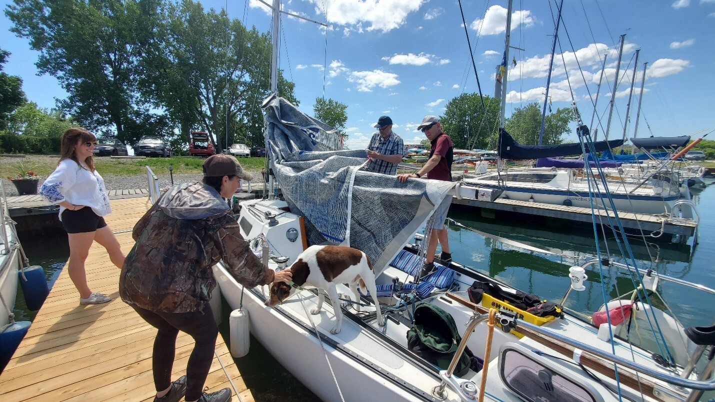 Several people and a dog standing around a sailboat that is docked