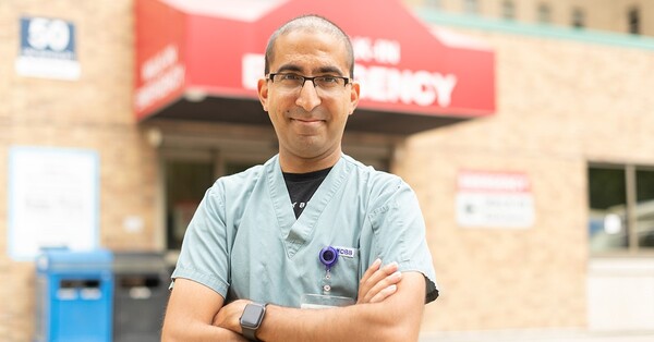 man in scrubs with arms crossed standing in front of ER entrance